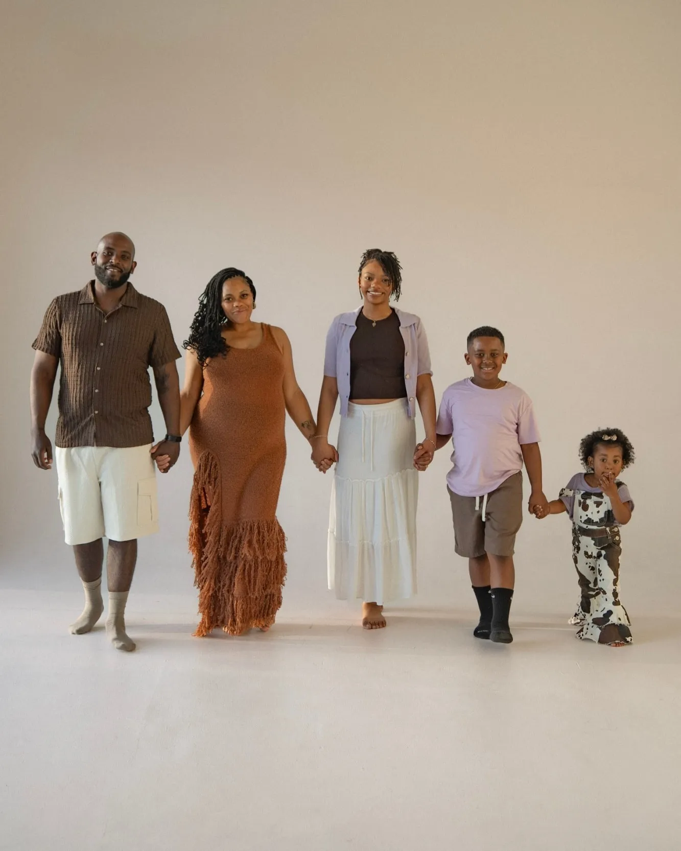 A family of five standing in a row, holding hands, in a bright studio with a soft cream backdrop.